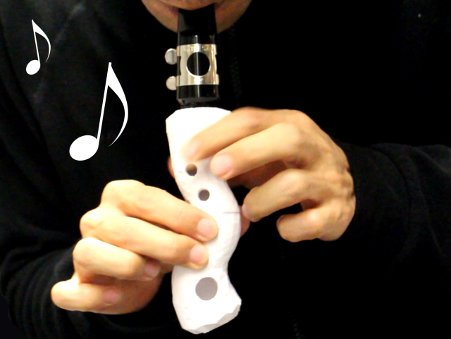 Image taken from the paper Printone: Interactive Resonance Simulation for Free-form Print-wind Instrument Design. The image shows a person playing a white free-form musical 3D-printed musical instrument that looks like a waved-shaped cylinder with holes of multiple diameters. This instrument was designed and its sound was simulated using the technique proposed in our paper.
